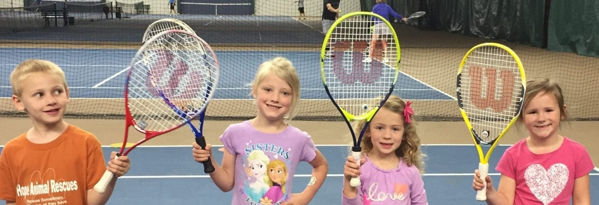 4 kids holding tennis rackets up
